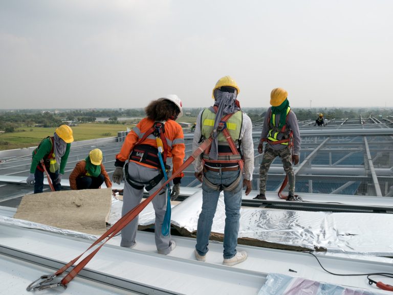 ConstructionWorkerWearingSafetyHarnessAndSafetyLineWorkingOn Commercial Roof Replacement Contractor
